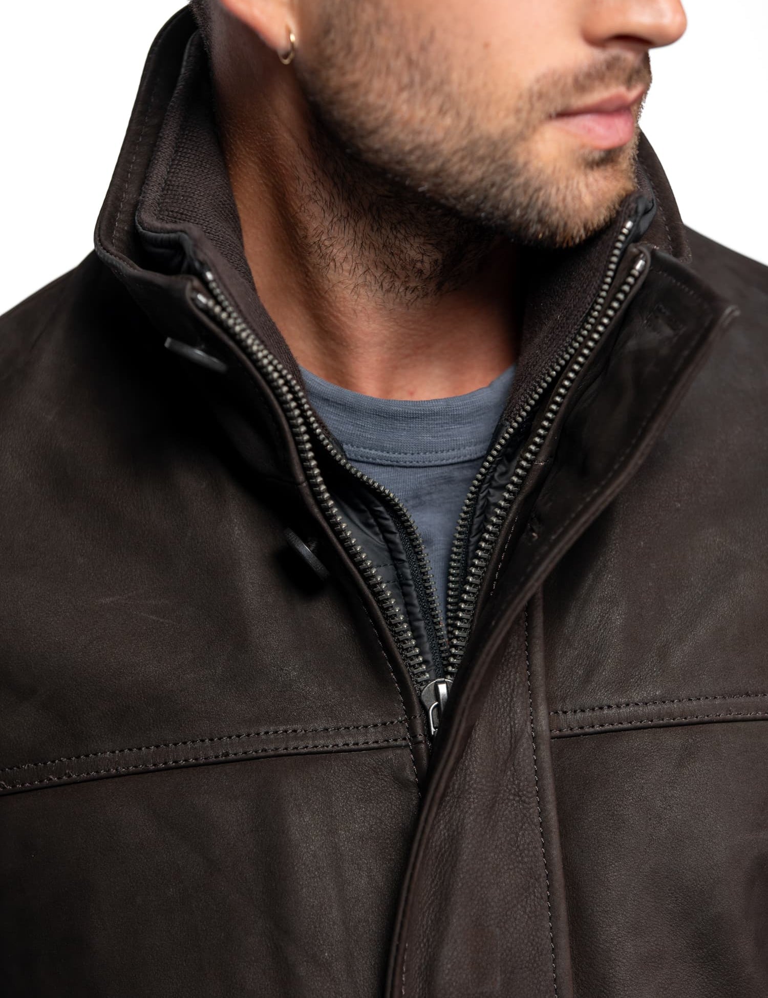 Man in a dark leather jacket with a high collar, wearing a blue shirt underneath. He has a beard and an earring, facing sideways.