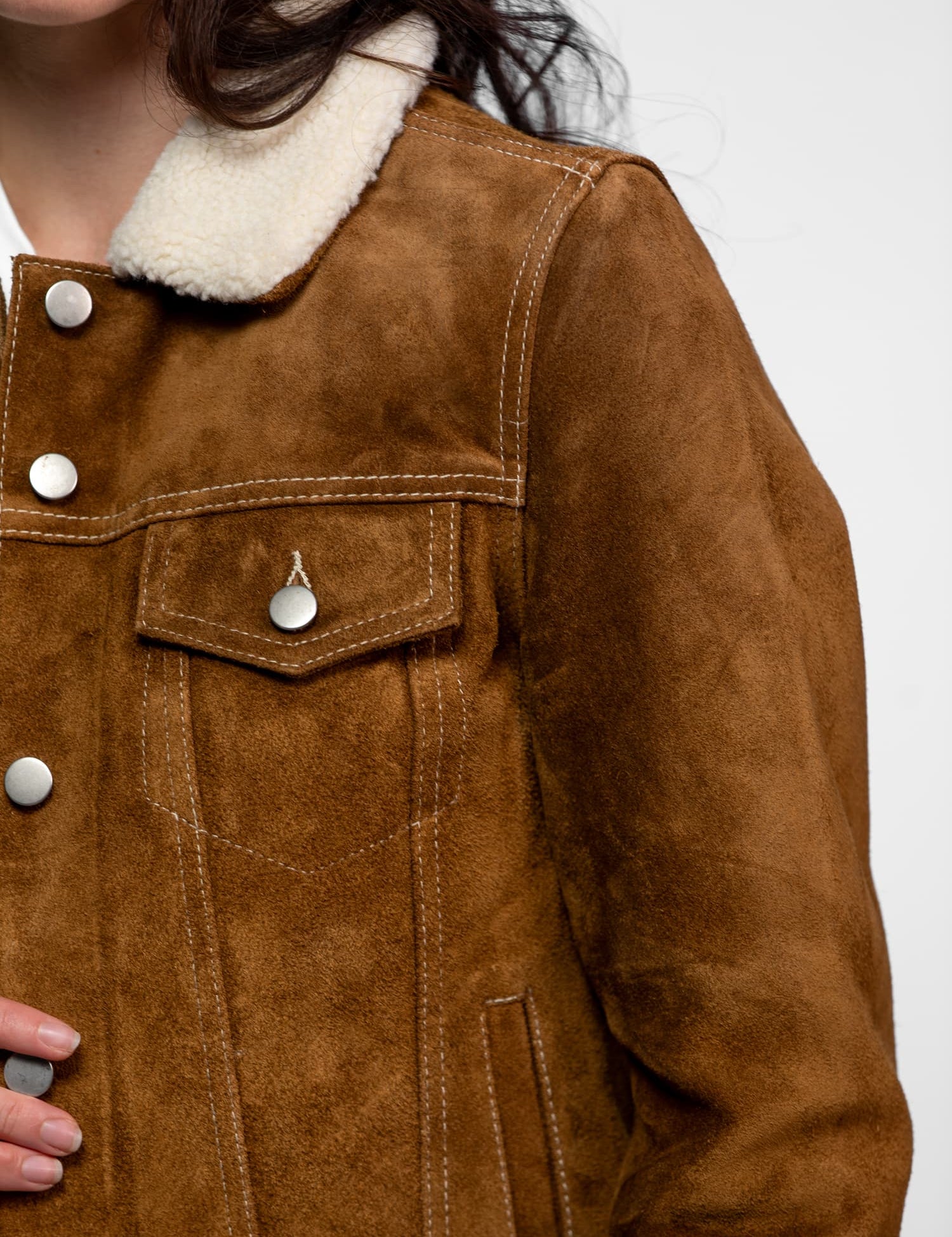 Close-up of a brown suede jacket with white shearling collar, silver buttons, and visible stitching, worn by a person.