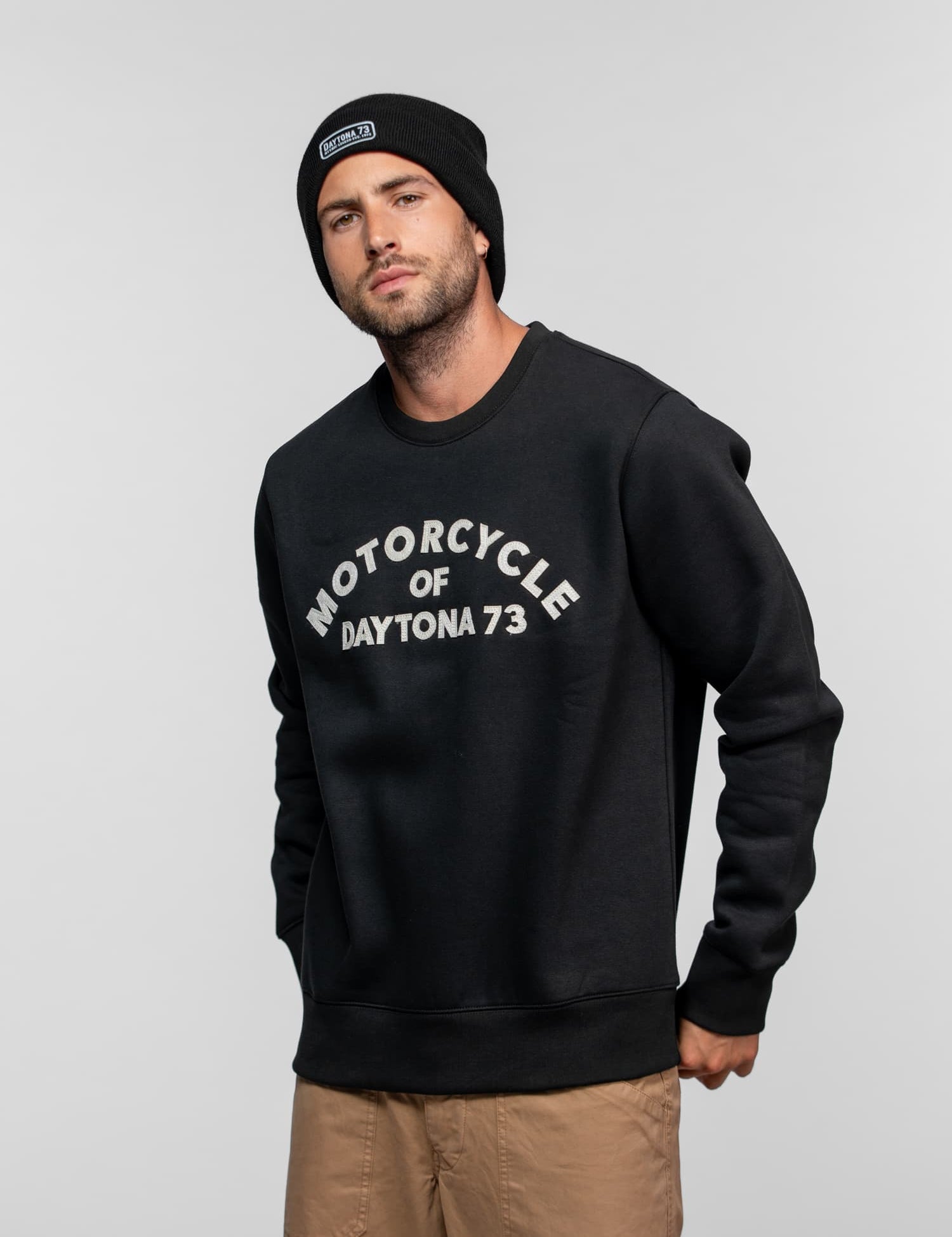 Homme portant un pull noir, un bonnet et un pantalon beige.