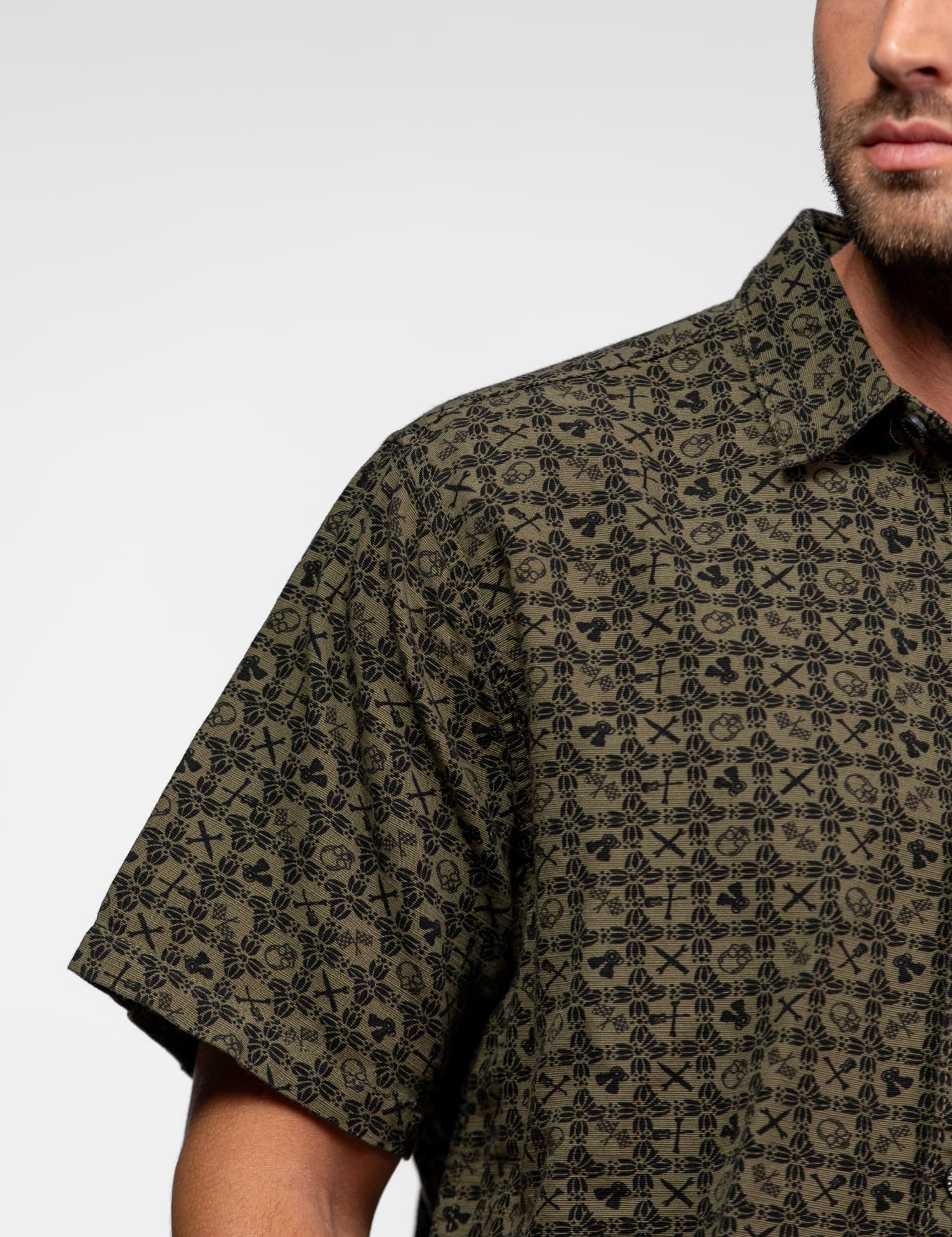 A man in a patterned short-sleeve shirt with a geometric design, showing part of his face and torso against a plain background.