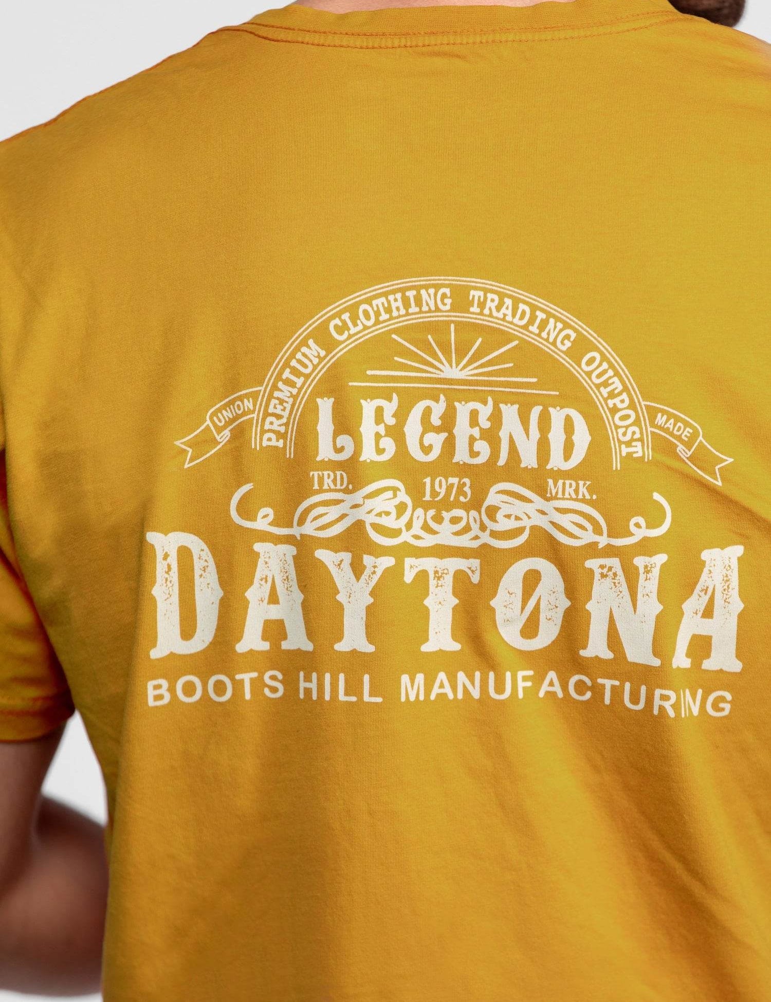 Back of a yellow shirt with "Legend Daytona Boots Hill Manufacturing" and vintage design in white text.