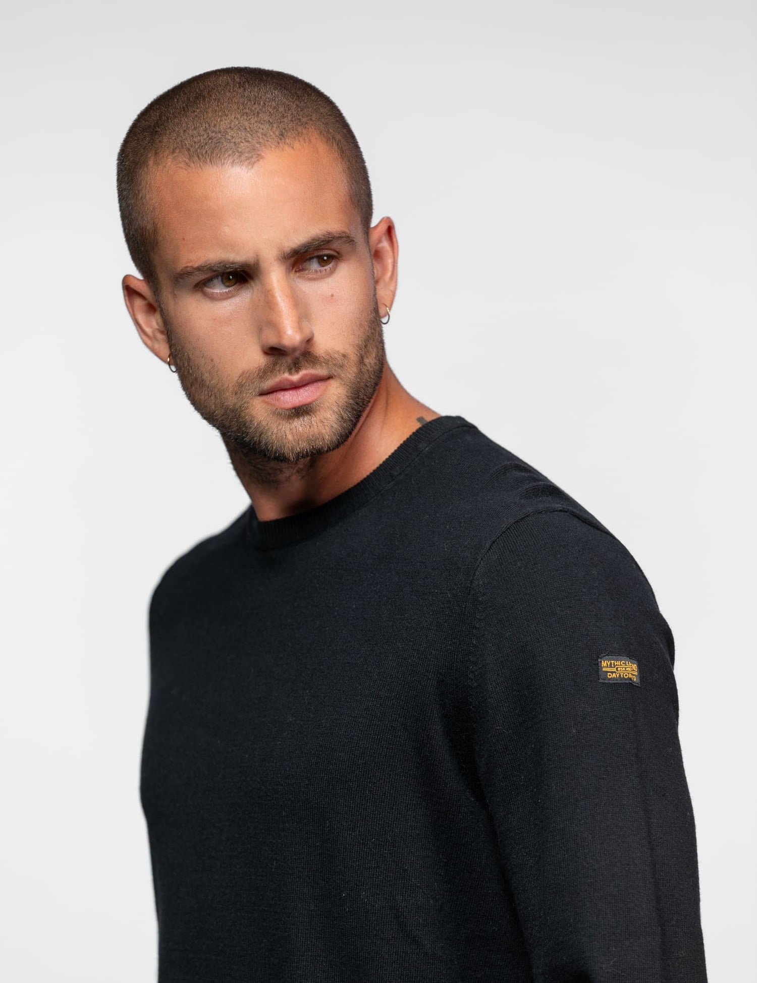 Homme de profil portant un pull noir à manches longues.