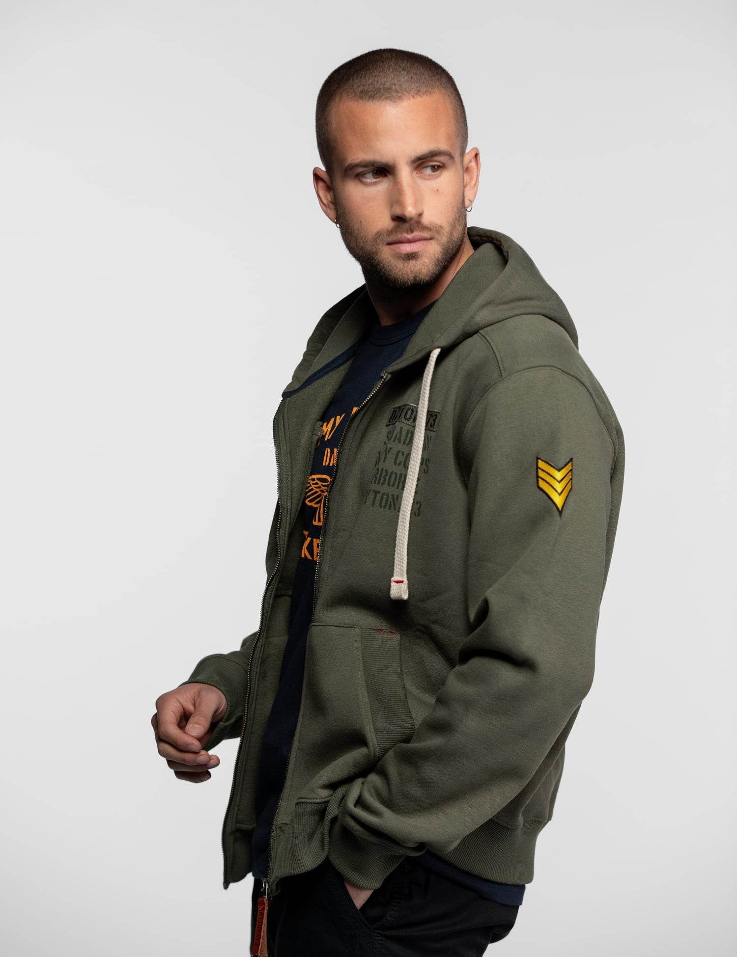 Veste à capuche olive green avec écusson jaune au bras.