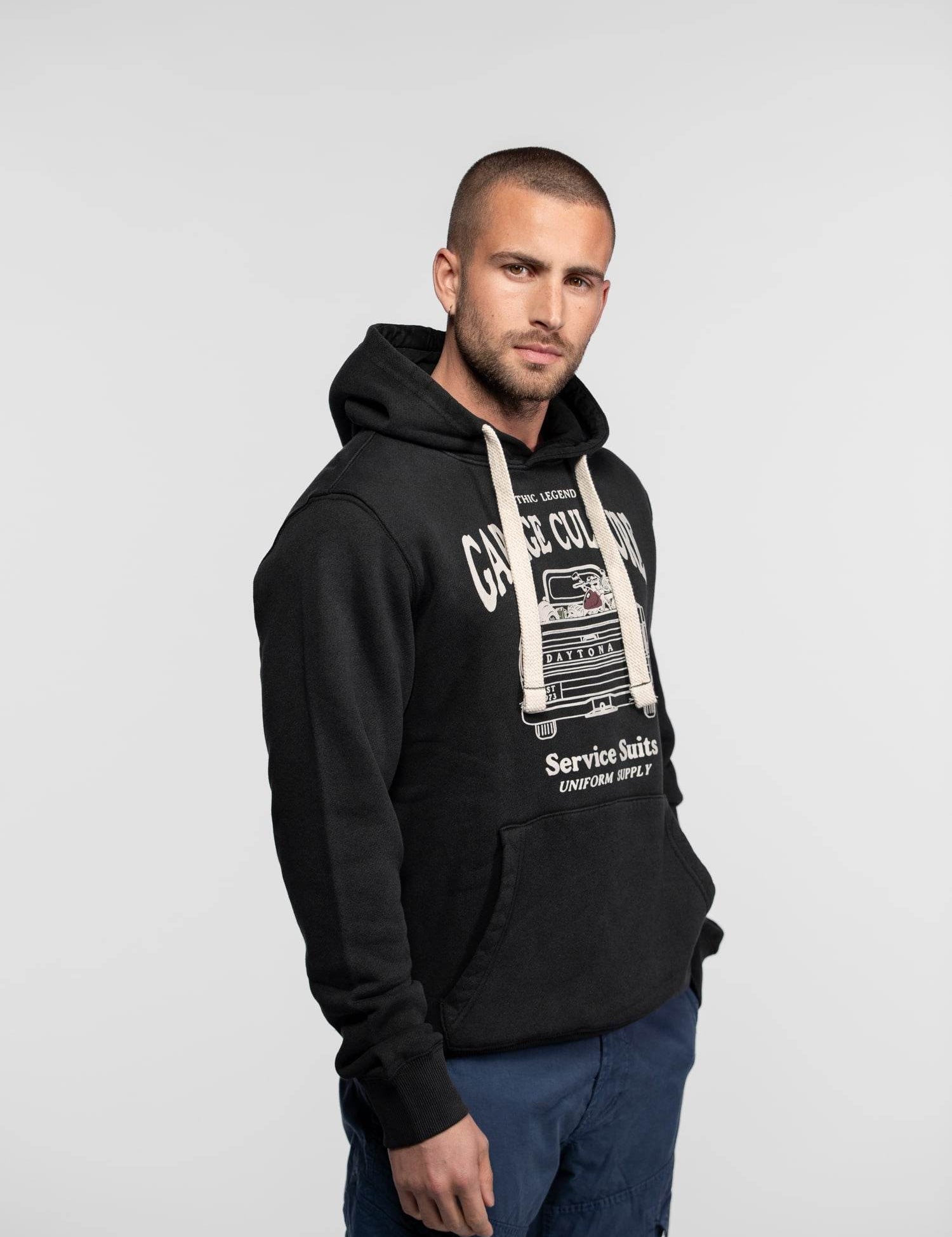 Man in a black hoodie with "Garage Culture" print, standing against a plain background, looking confidently at the camera.