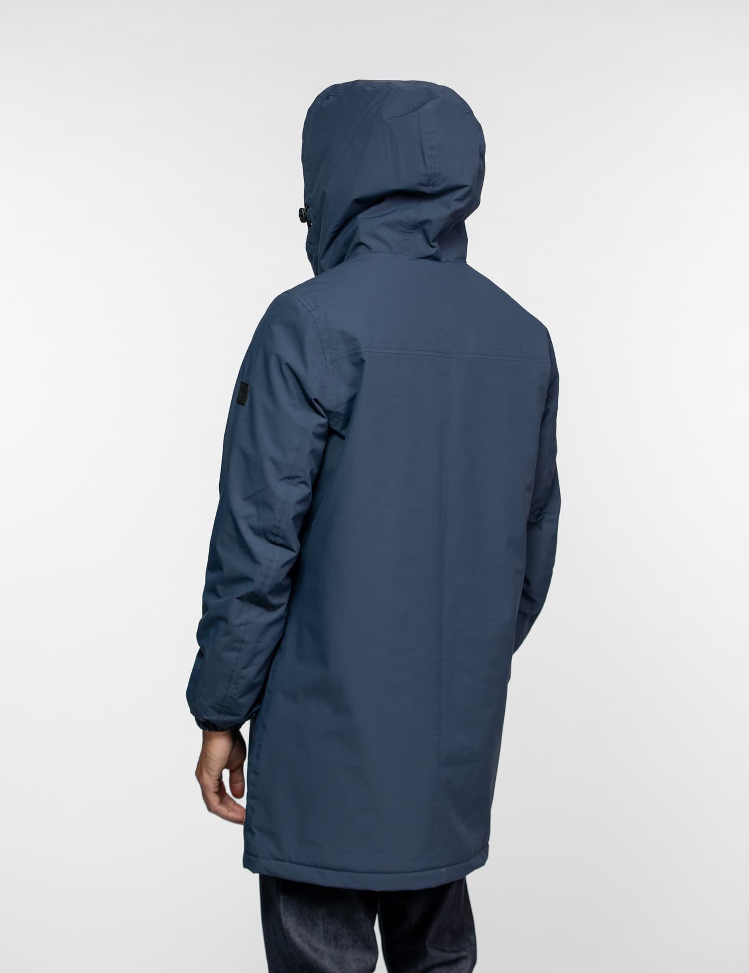 Person in a blue hooded jacket facing away, wearing dark jeans, against a plain white background.