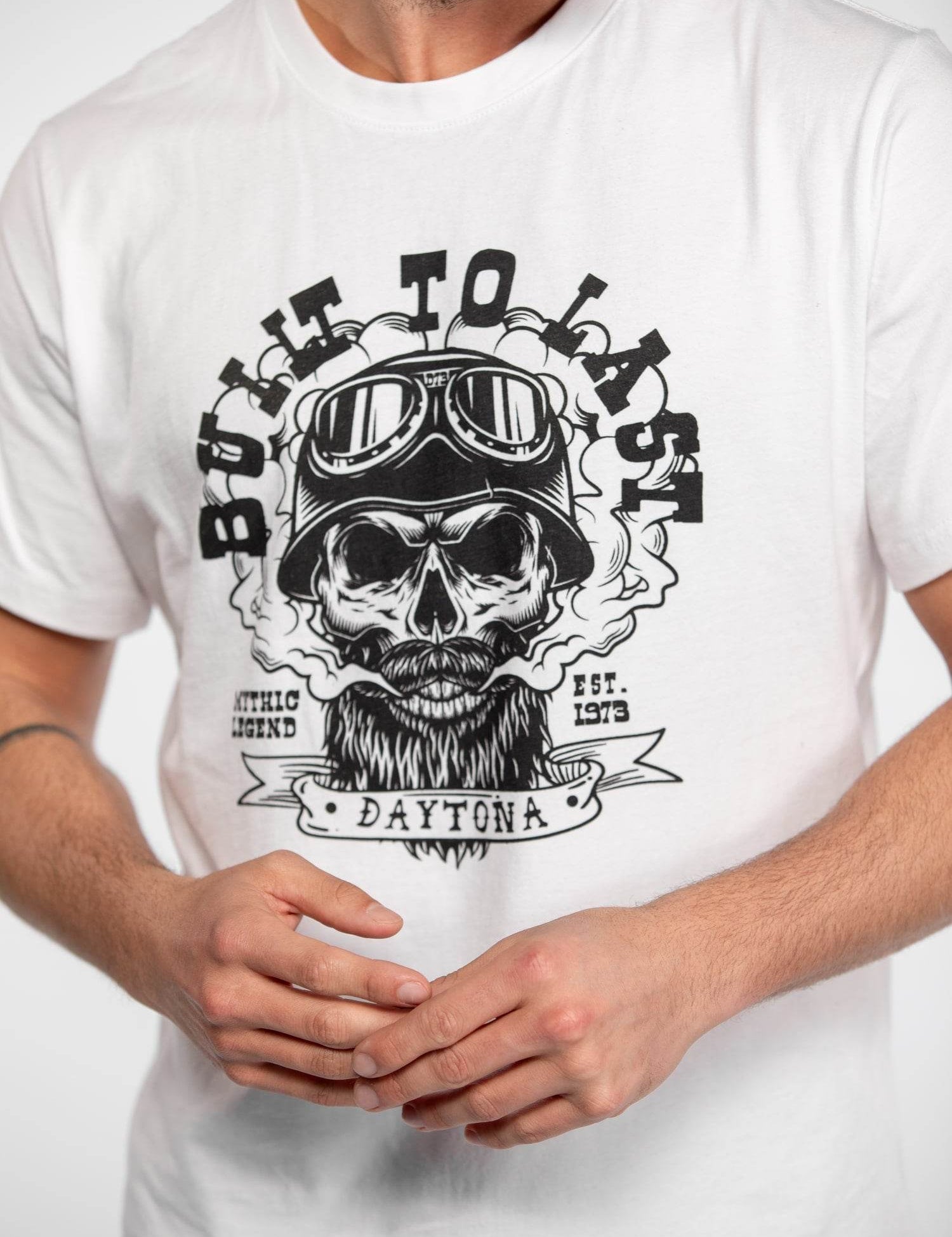 A person wears a white shirt with a "Built to Last" skull design, featuring goggles and "Daytona" text, emphasizing durability.