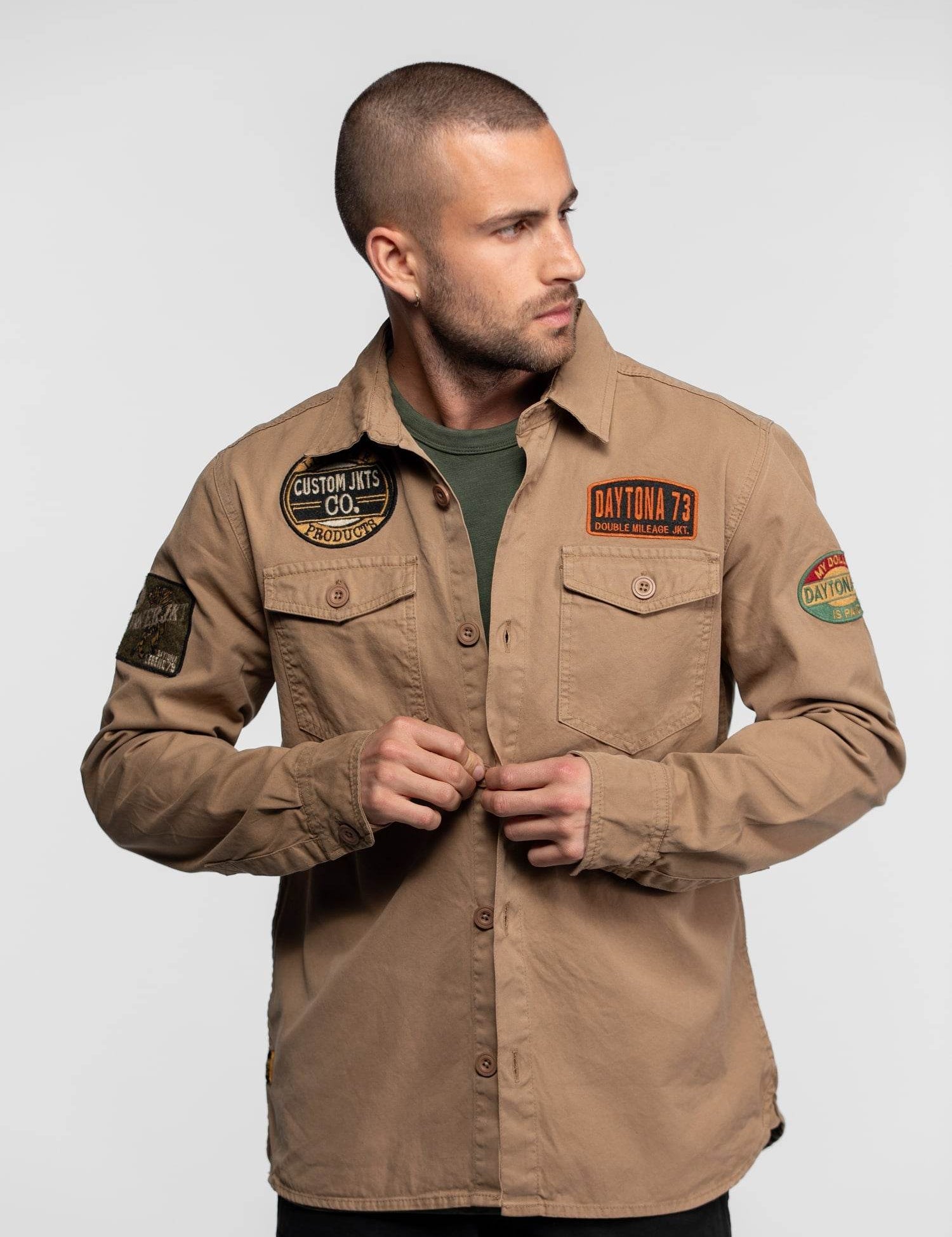 Homme portant une chemise beige avec des écussons.