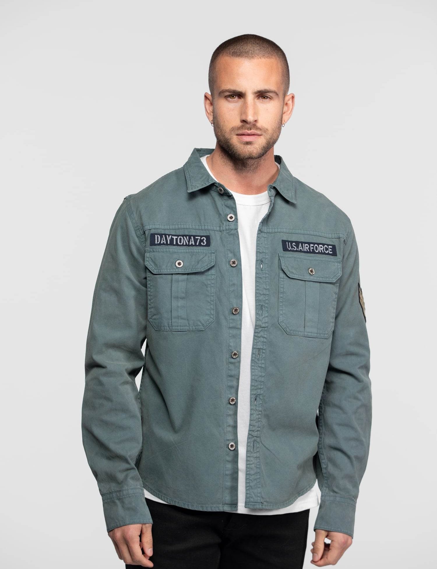 Man in green "U.S. Air Force" shirt stands confidently, wearing a white tee underneath, against a plain background.