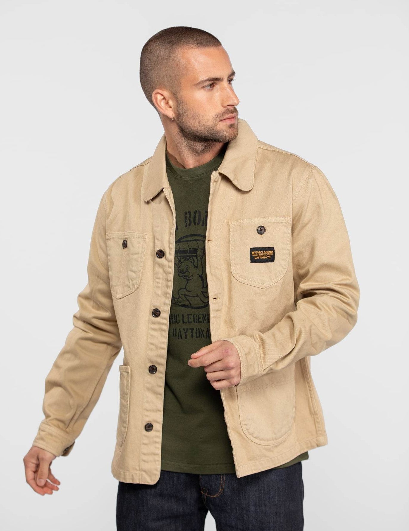Veste de travail beige avec boutons et écusson noir.