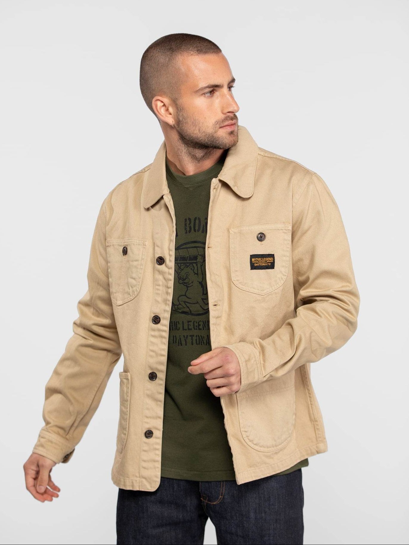Veste de travail beige avec boutons et écusson noir.