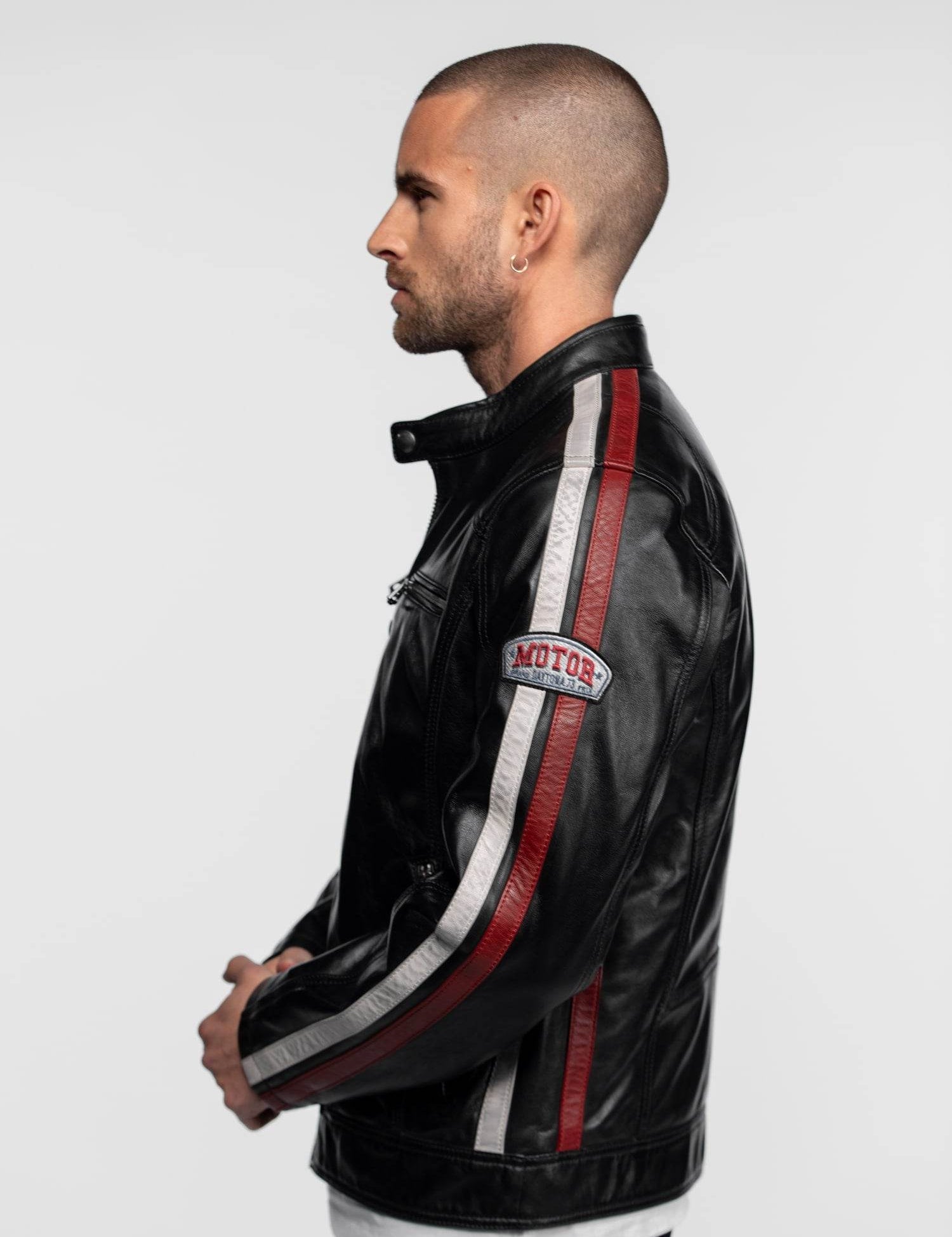 Man in profile wearing a black leather jacket with red and white stripes, "Motor" patch on sleeve, against a plain background.