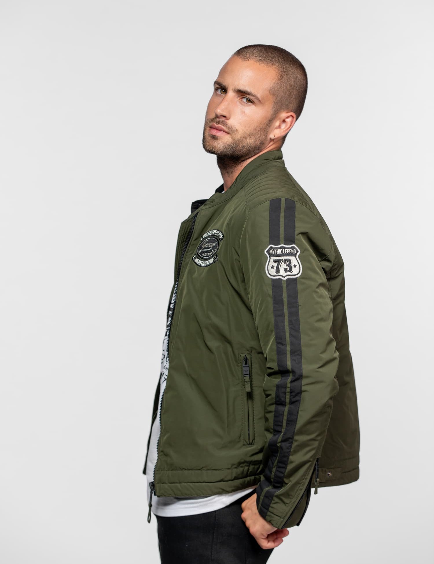 Blouson olive green avec écussons, bandes noires et fermetures éclair.