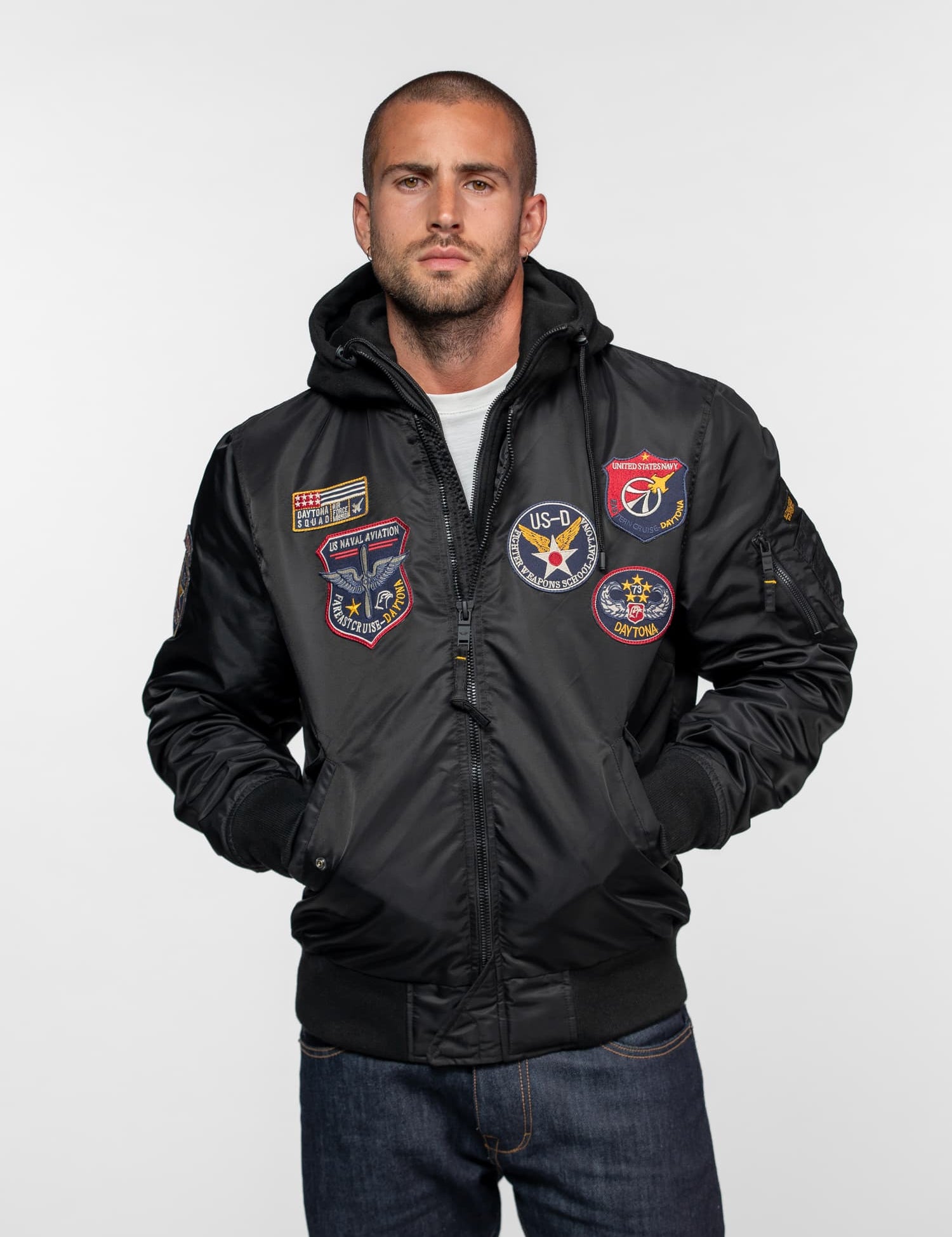 Blouson aviateur noir à capuche avec de multiples écussons brodés.