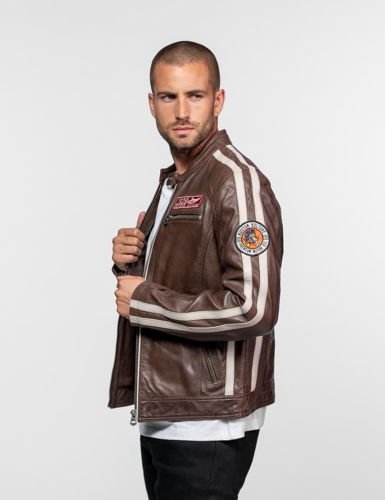 Homme en veste marron avec écussons et jean noir.