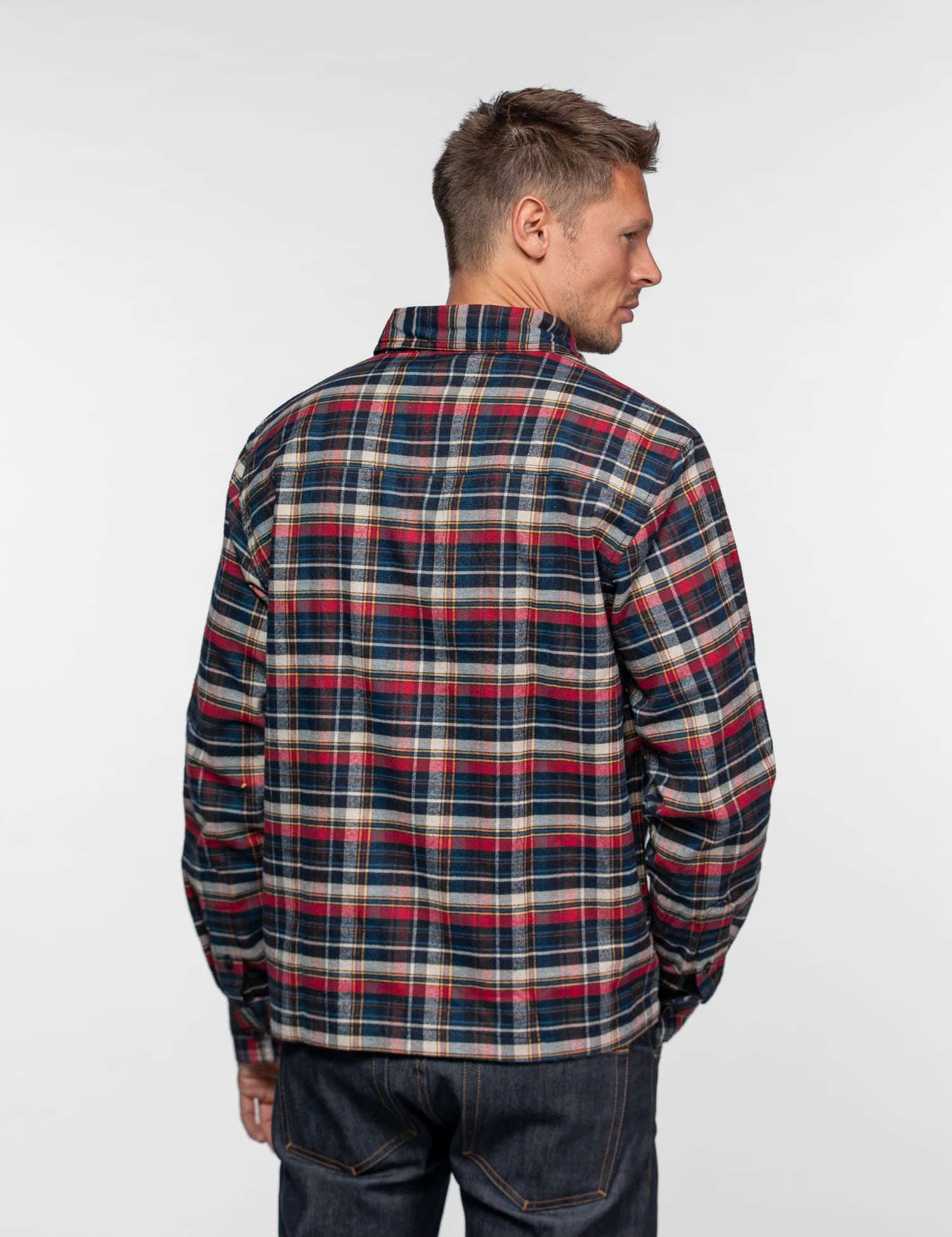 Man in a plaid shirt and jeans, viewed from behind, against a plain white background.