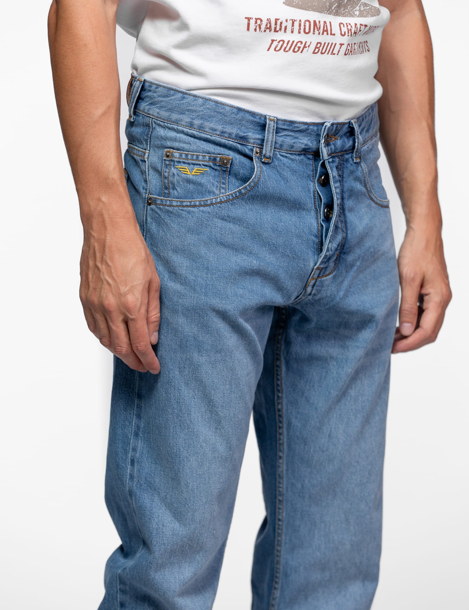 Man in blue jeans and a white graphic tee stands against a plain background, showcasing casual fashion with a relaxed fit.
