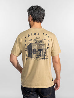 Homme en chemise beige avec le slogan « Ride It, Fix It, Repeat » et un dessin de garage, de dos, sur fond uni.