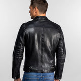 Un homme en veste de cuir noire et jean bleu, de dos, sur fond uni, mettant en valeur les détails du dos de sa veste.
