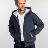 Homme en sweat-shirt bleu marine sur chemise blanche, regardant sur le côté. Mains dans les poches, pose décontractée, fond neutre.