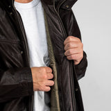 Un homme en chemise blanche ouvre la fermeture éclair d'une veste en cuir marron foncé, révélant une doublure intérieure matelassée, sur un fond neutre.