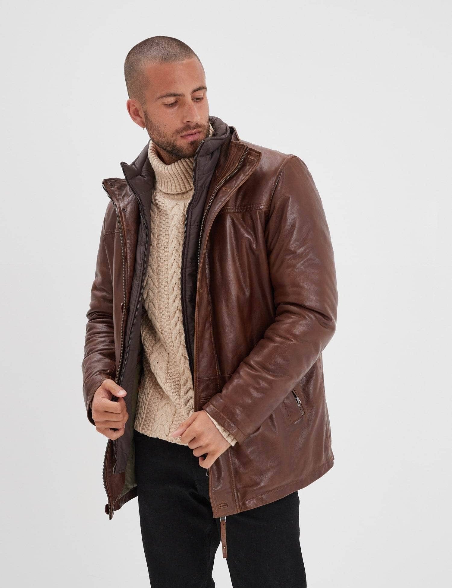 Homme en manteau marron, pull torsadé et col roulé.