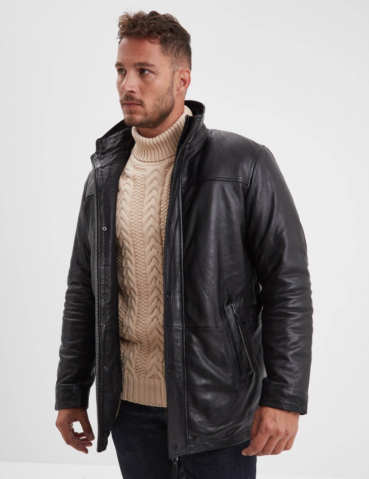 Homme portant un manteau noir sur un pull beige.
