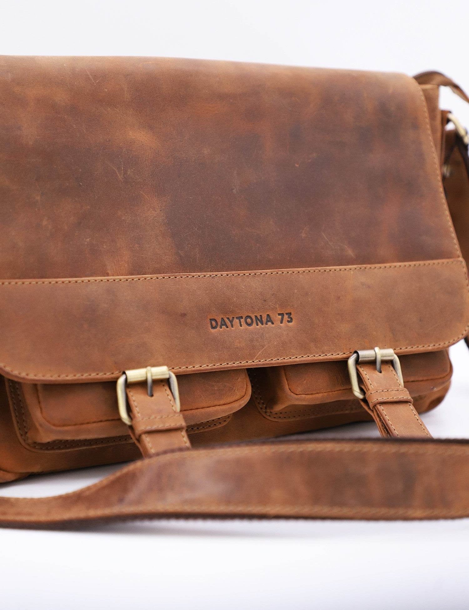 Brown leather messenger bag with "DAYTONA 73" embossed, featuring two front pockets and a long adjustable strap.