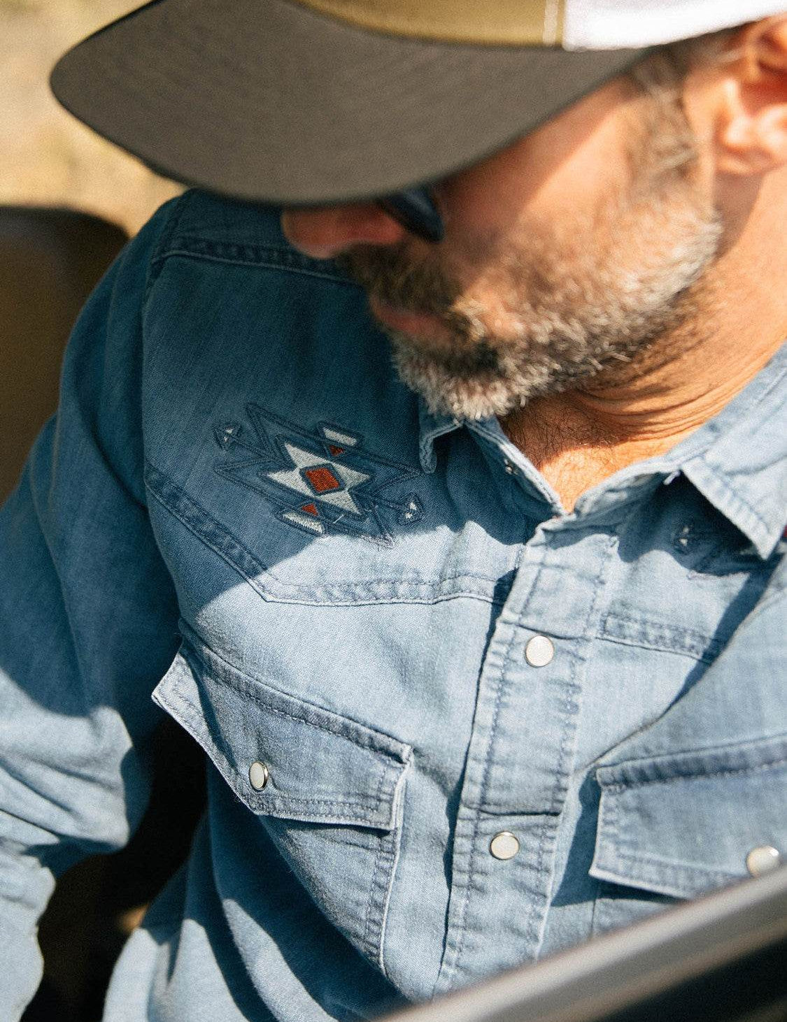 Homme en chemise en jean avec broderie et casquette.