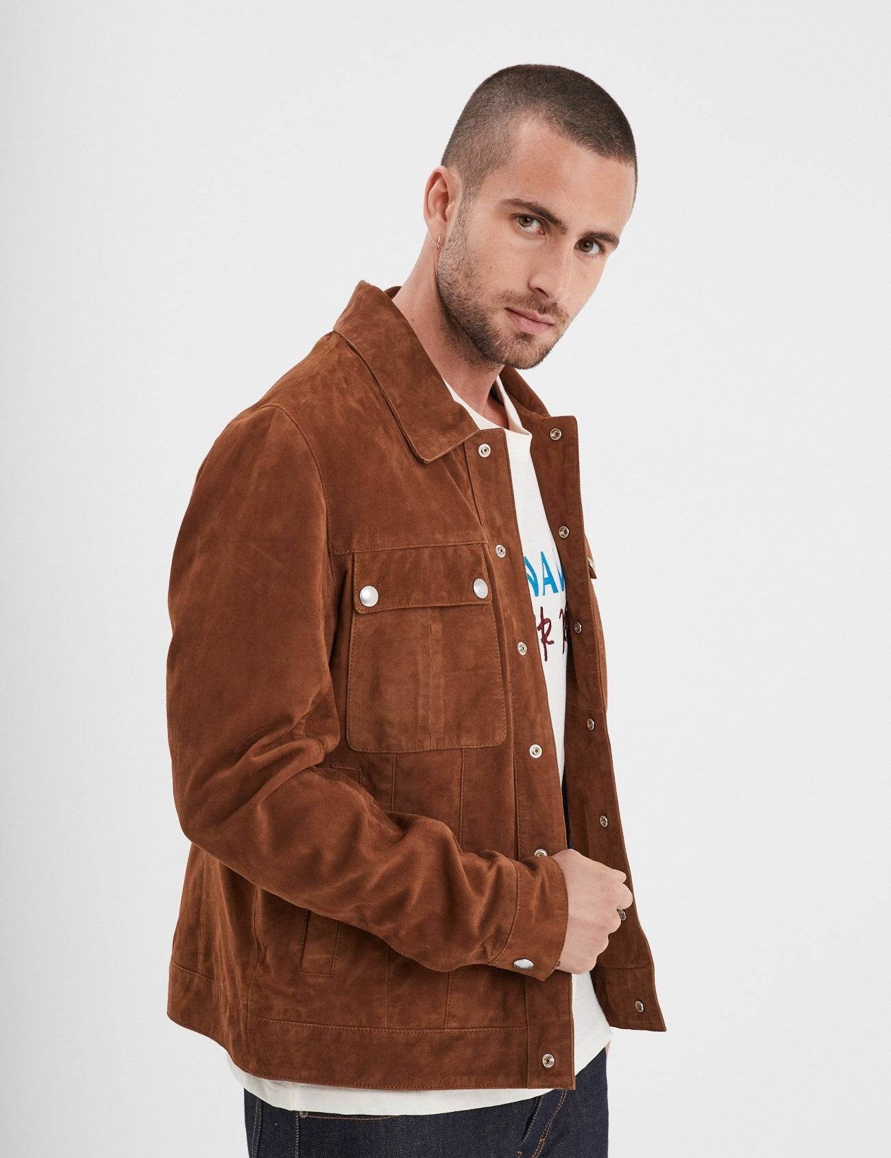 Man in a brown suede jacket over a graphic tee, looking confidently at the camera against a plain white background.
