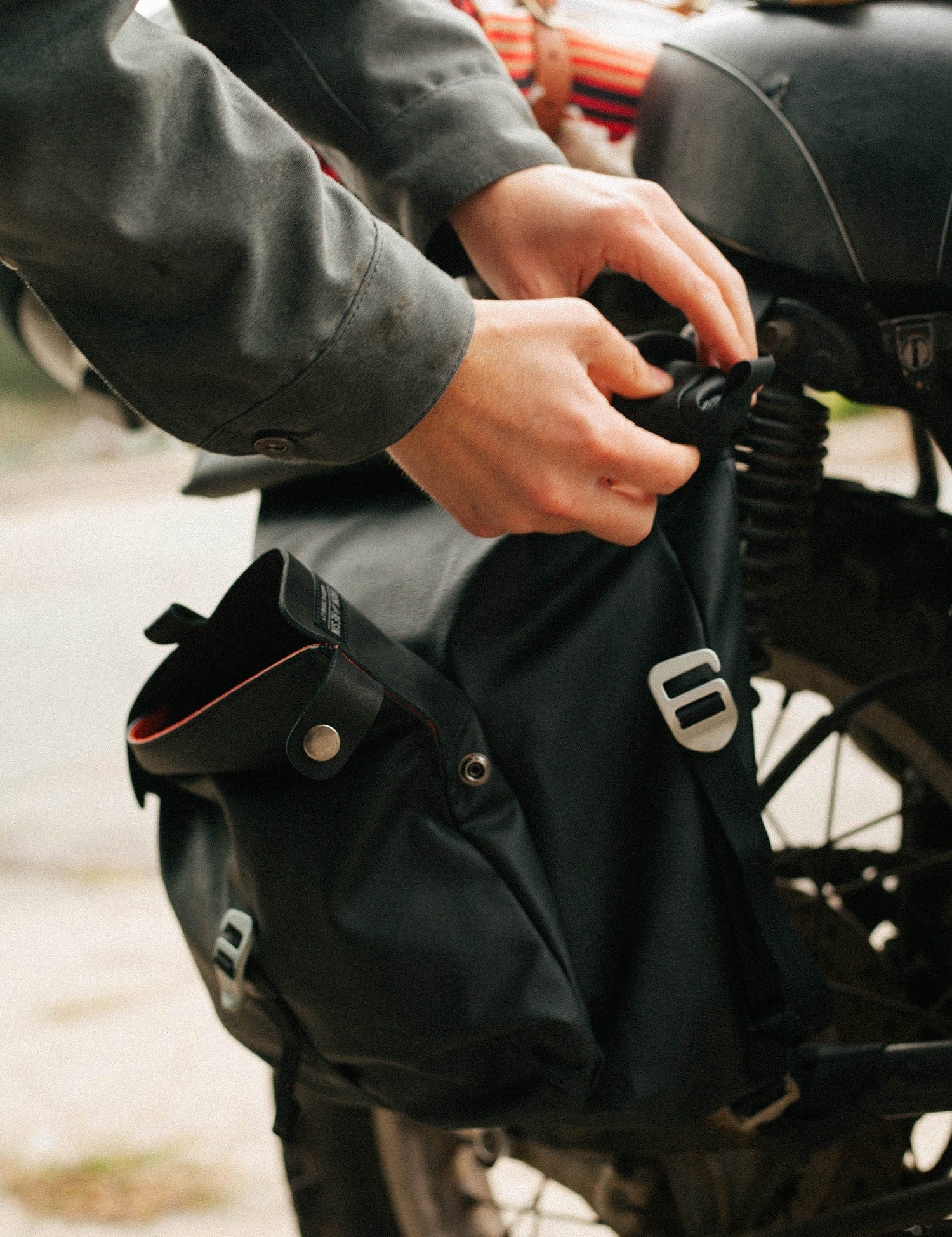 Hands securing a black saddlebag onto a motorcycle, highlighting the bag's sleek design and sturdy buckles.