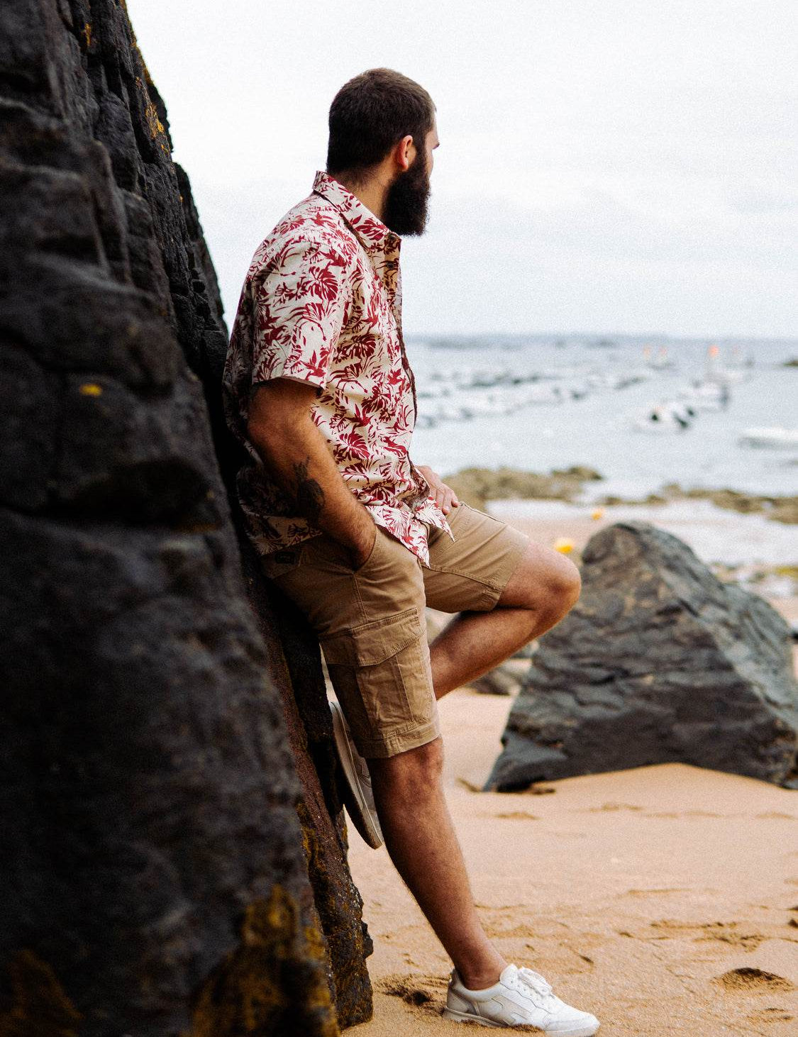 Homme barbu de profil en chemise fleurie sur la plage.