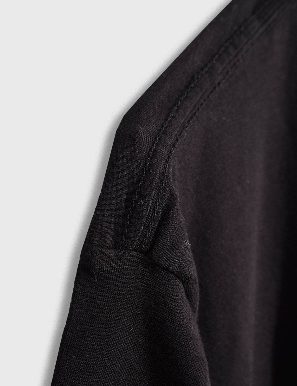 Détail d'une couture d'épaule sur un vêtement noir.